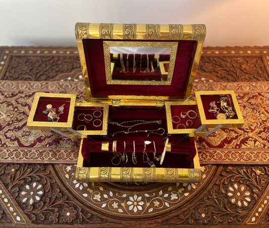 Decorative jewelry box with gold accents and jewelry on a patterned surface