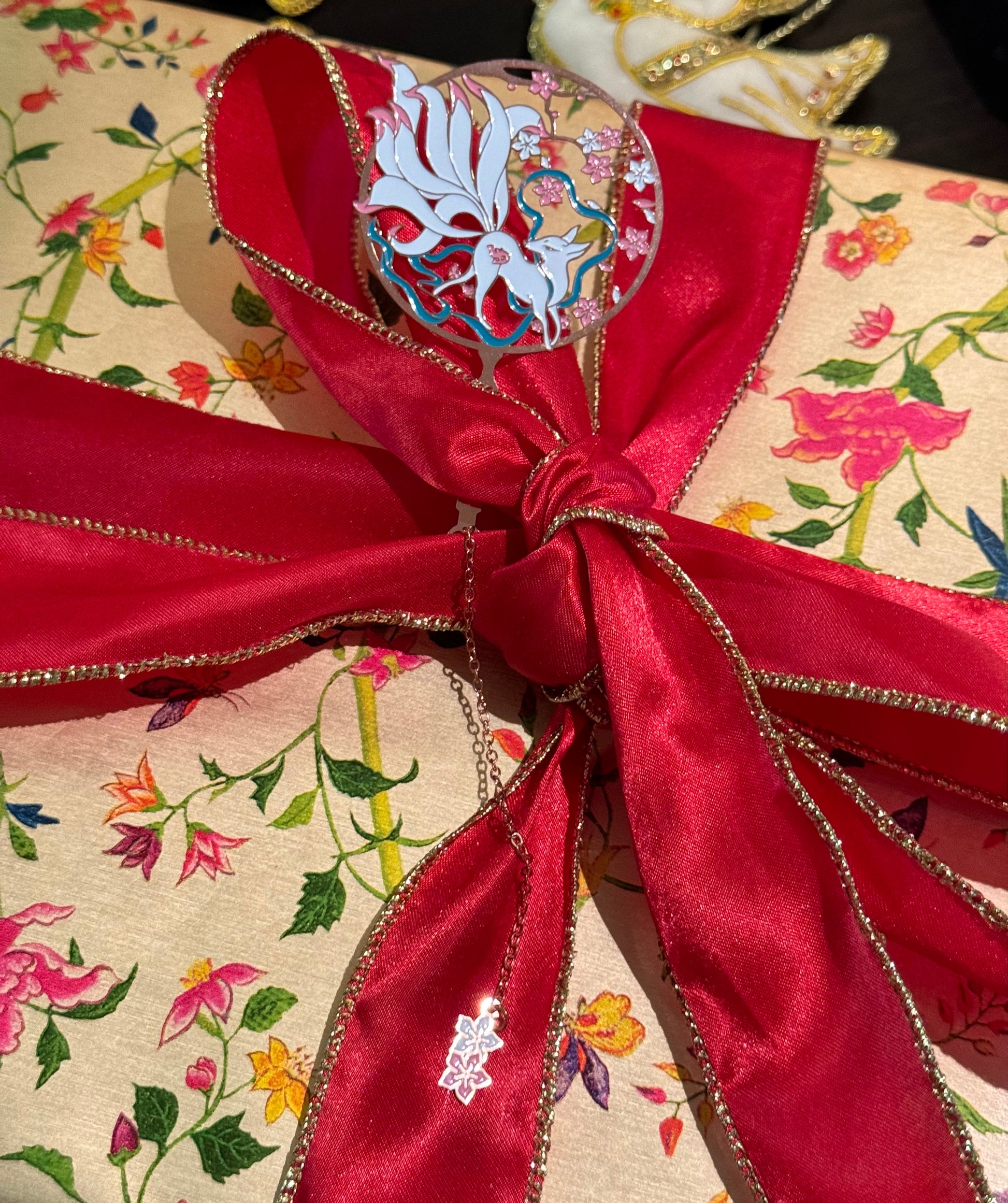 Nine Tailed Fox Metal Bookmark with Sakura Charm lying on a gift wrapped box with a big red bow