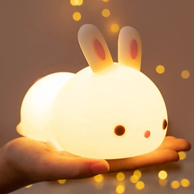 Cute rabbit-shaped night light held in a hand with a warm glow against a blurred background.