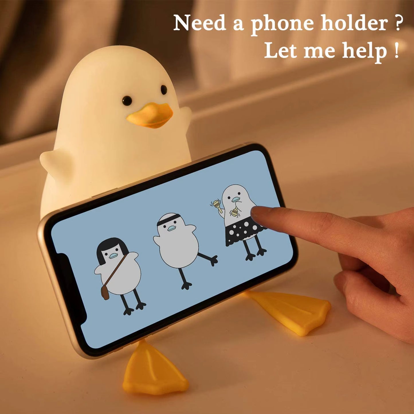 Yellow duck-shaped phone holder with a smartphone displaying cartoon penguins on a beige surface.