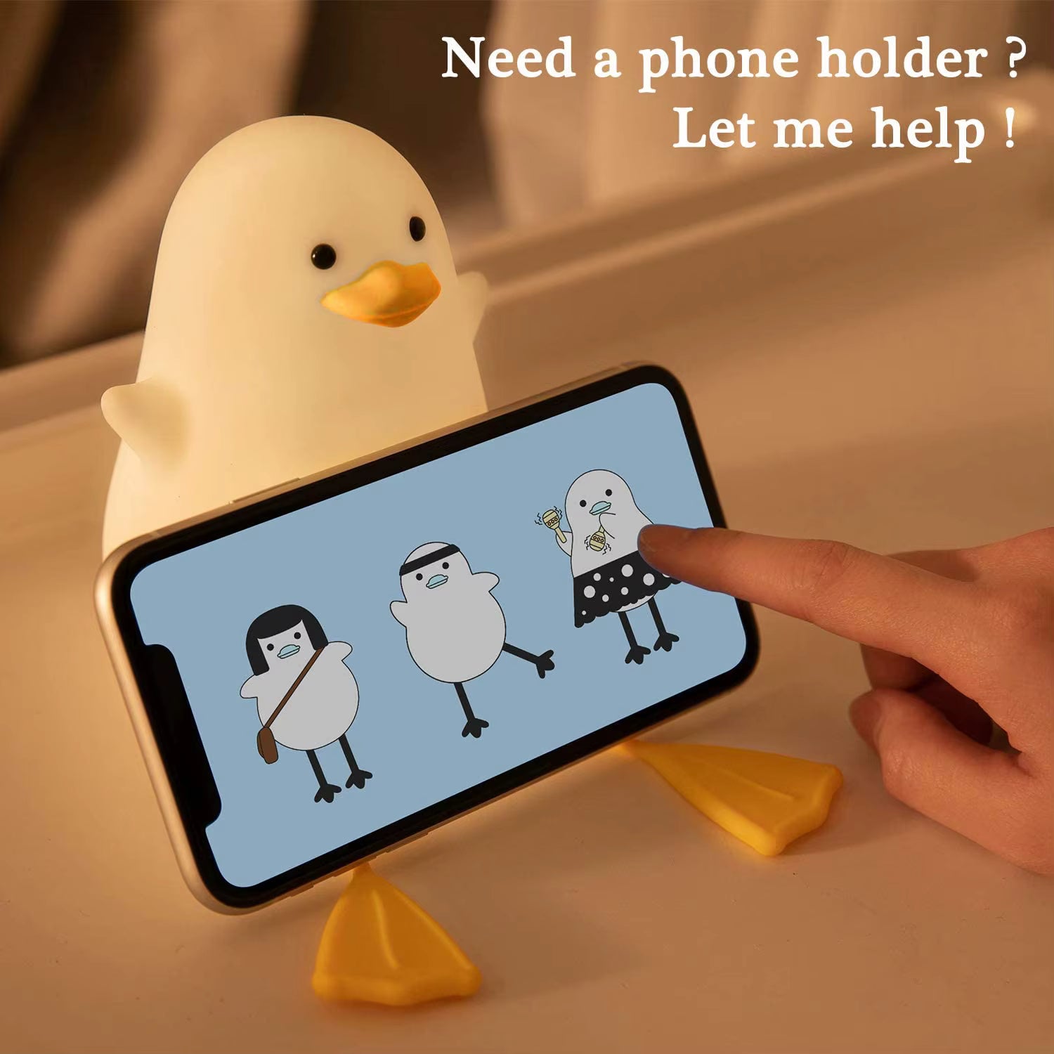 Yellow duck-shaped phone holder with a smartphone displaying cartoon penguins on a beige surface.