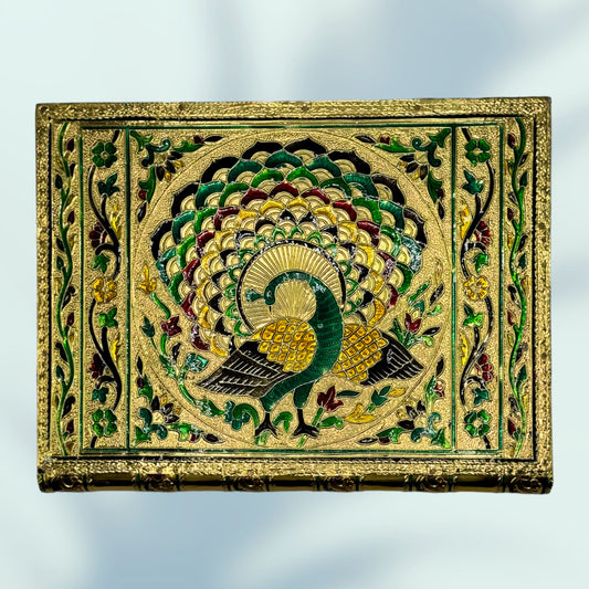 top view of the cover of the regal peacock meenakari box to show the handmade crafting technique where colored enamel is filled into the etched design of the peacock with flourishes framing the design 