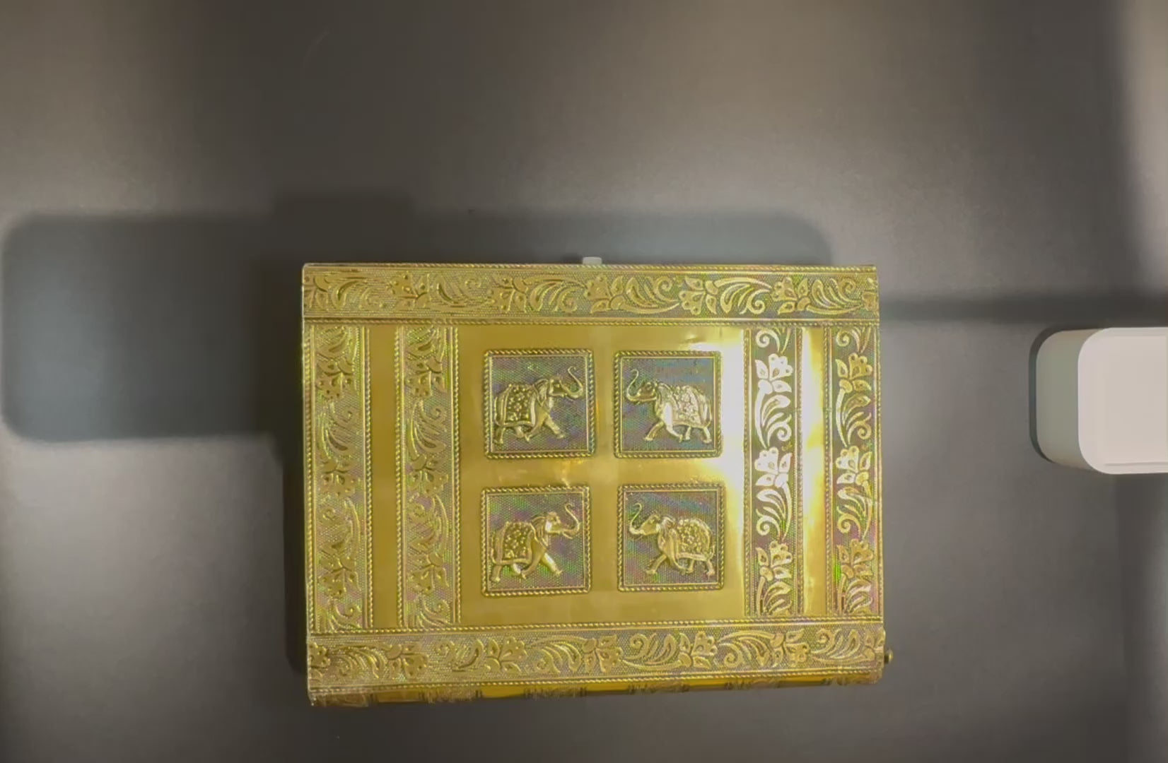 video of opening the gold vintage Indian Jewelry box that shows how the trays fan out and the dowel for bangles is removed. It also shows the latch that closes the box and the edge of the book like design