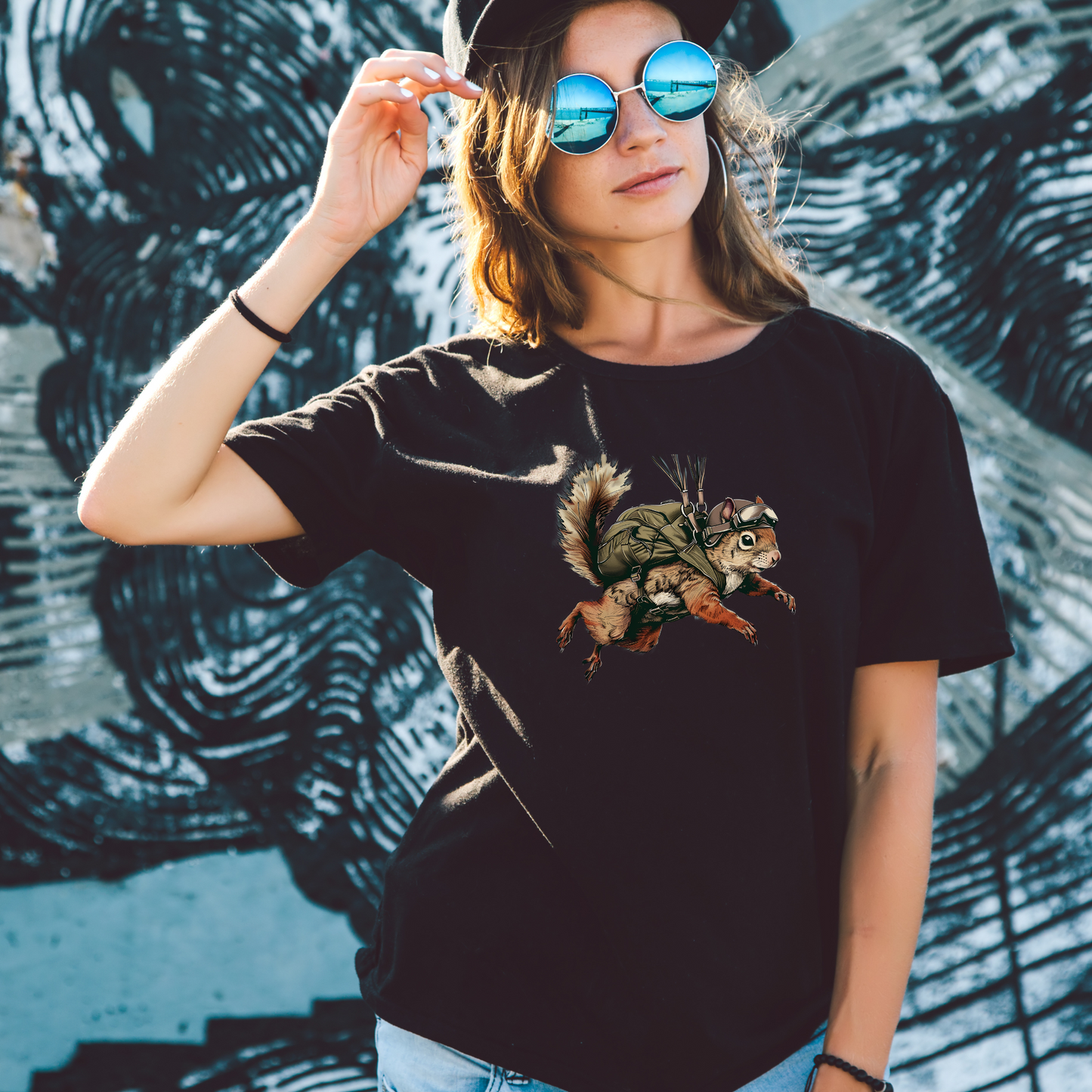 Person wearing a black t-shirt with a graphic design of a frog and squirrel, standing against a textured wall.