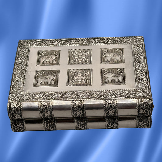 An Indian silver-toned metal jewelry box with embossed floral borders and  elephant motifs on the lid, shown against a blue gradient background.